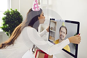 Young woman having online birthday party with her boyfriend and kissing the computer screen