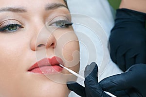 Young woman having permanent makeup on her lips at the beautician salon