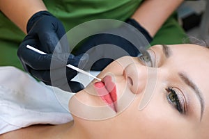 Young woman having permanent makeup on her lips at the beautician salon