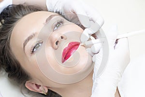 Young woman having permanent makeup on her lips at the beauticians salon