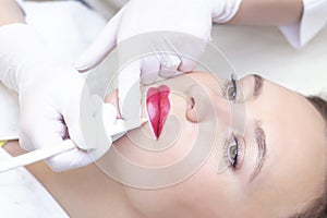 Young woman having permanent makeup on her lips in a cosmetologists salon.