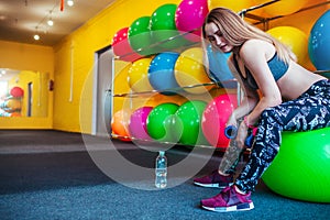 Young woman having rest at the gym. Muscular female relaxes and smiles after training while sitting on the ball.