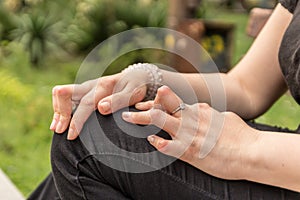 Young woman having rheumatoid arthritis takes a rest sitting on a bench at a park. Hands and legs are deformed. She feels pain.