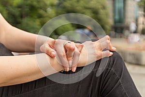 Young woman having rheumatoid arthritis takes a rest sitting on a bench at a park. Hands and legs are deformed. She feels pain.