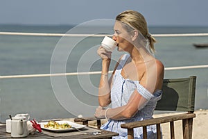 Young woman having romantic breakfast in hotel restaurant during sunrise near sea waves on the tropical beach, close up. Concept