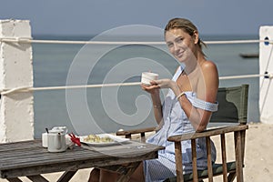 Young woman having romantic breakfast in hotel restaurant during sunrise near sea waves on the tropical beach, close up. Concept