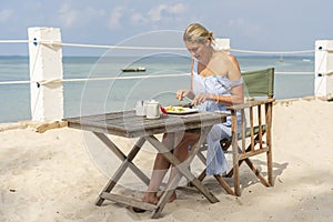 Young woman having romantic breakfast in hotel restaurant during sunrise near sea waves on the tropical beach, close up. Concept
