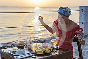 Young woman having romantic dinner in hotel restaurant during sunset near sea waves on the tropical beach, close up