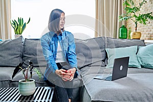 Young woman having video call sitting on sofa at home, using laptop