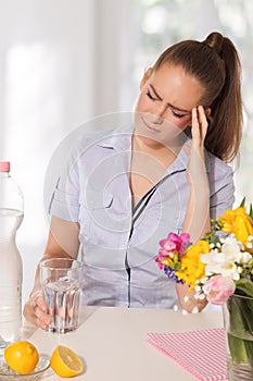 Young woman with headache holding a glass of water