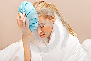 Young woman with headache, holding an ice-bag next to her forhead