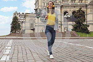 Young woman with headphones crossing street. Traffic rules and regulations