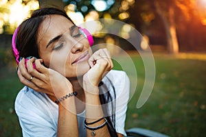 Young woman with headphones enjoy music outdoors. Girl repose or lie down at sunset on green grass.
