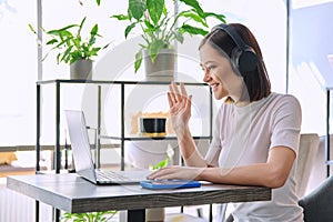 Young woman in headphones having work video chat conference call, using laptop in cafe