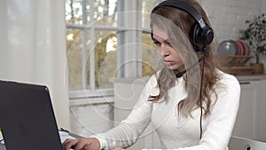 A young woman in headphones with a headset works at a laptop. Distance learning or work, call center operator working