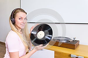 Young woman with headphones listens to music from vinyl records at home