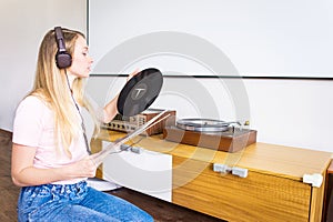 Young woman with headphones listens to music from vinyl records on a turntable at home.