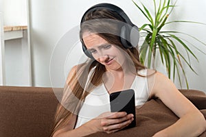 Young woman in headphones looks into smartphone and grins