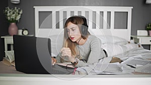 Young woman with headphones lying on the bed using notebook. Freelance, work at home, work outside the office.