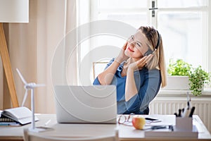 Young woman with headphones sitting at the desk indoors in home office.