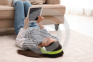 Young woman with headphones and tablet listening to music on floor