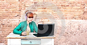 Young woman with headphones using laptop at house office - Remote smart working and technology concept due to isolation emergency photo