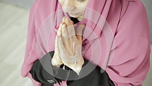 Young woman in headscarf is praying. close-up female hands holding chain with a cross