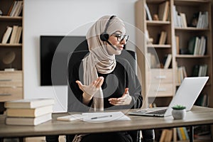 Young woman in headset having video call with partners, working process at office.