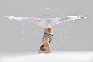 Young woman in headstand exercise, grey studio background