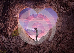Young woman in heart shape cave towards the beautiful sky
