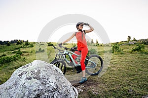 A young woman in a helmet and with a backpack stands with a bicycle and looks at the mountains