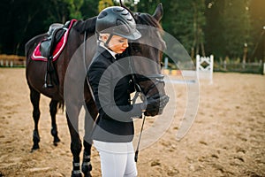 Young woman in helmet hugs horse, horseback riding