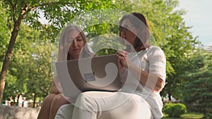 Young woman helping her old retired mother on a laptop sitting in a park. Concept of Age Inclusivity