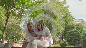 Young woman helping her old retired mother on a laptop sitting in a park. Concept of Age Inclusivity