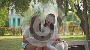 Young woman helping her old retired mother on a laptop sitting in a park. Concept of Age Inclusivity