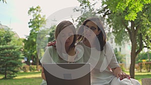 Young woman helping her old retired mother on a laptop sitting in a park. Concept of Age Inclusivity. Slow motion shot