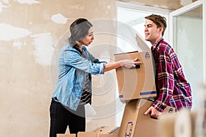 Young woman helping her partner to carry two boxes while moving in