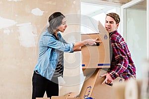 Young woman helping her partner to carry two boxes while moving into a new home