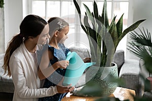 Young woman helping little kid girl watering domestic plants.