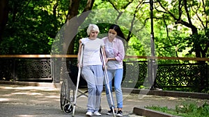 Young woman helping old lady walking on crutches, hip fracture rehabilitation