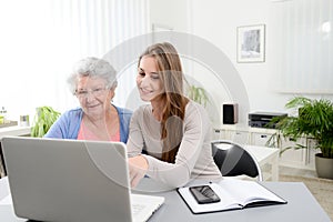 Young woman helping an old senior woman doing paperwork and administrative procedures with laptop computer at home