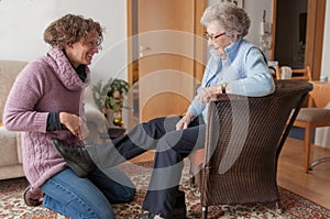 Young woman helping senior lady taking on her shoes