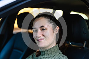 Young woman in her 30\'s with dark hair and attractive smiling inside her car looking at camera.