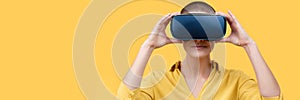 Young woman in her 30s using virtual reality goggles. Woman wearing VR headset isolated over yellow banner. VR experience.