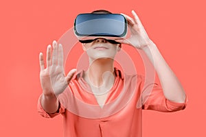 Young woman in her 30s using virtual reality goggles. Woman wearing VR headset  over coral background. VR experience.