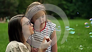 Young woman and her 6 year old daughter are blowing rainbow soap bubbles. Fun family vacation.