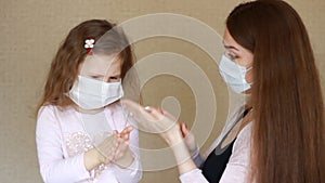 Young woman and her baby girl in medical mask using liquid hand sanitizer during quarantine. Mother and daughter using