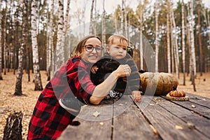 Young woman and her baby son in autumn park, boy playing with helloween pumpkin and eating pumpkin bun.