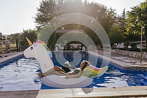 young woman and her border collie dog standing on an inflatable toy unicorn at the swimming pool. Summertime, fun and lifestyle