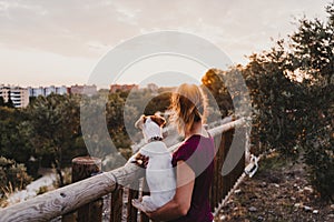 young woman and her cute small jack russell terrier dog watching sunset outdoors in a park. Golden hour. Love for animals concept